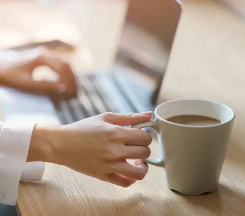 Kvinde arbejder ved computer med en kop filterkaffe i hånden